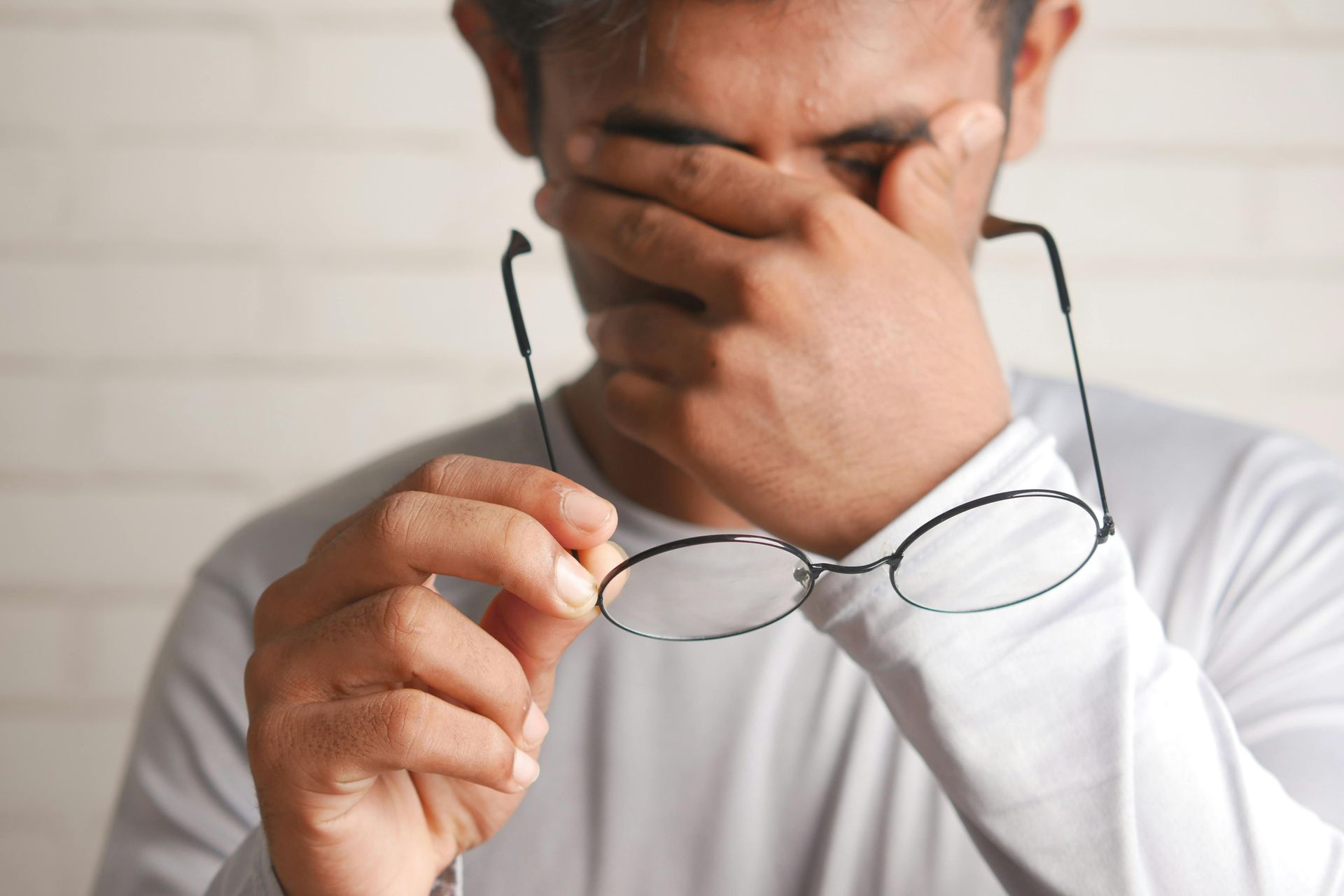 Person with glasses in hand, covering face with one hand, appearing stressed at a desk