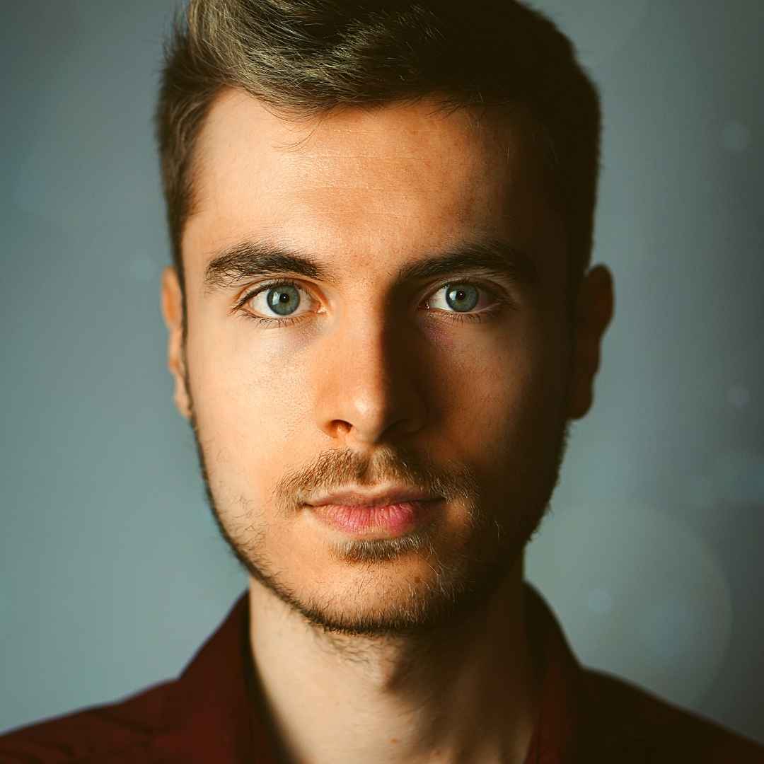 A close up of a man 's face with a beard wearing a red shirt.