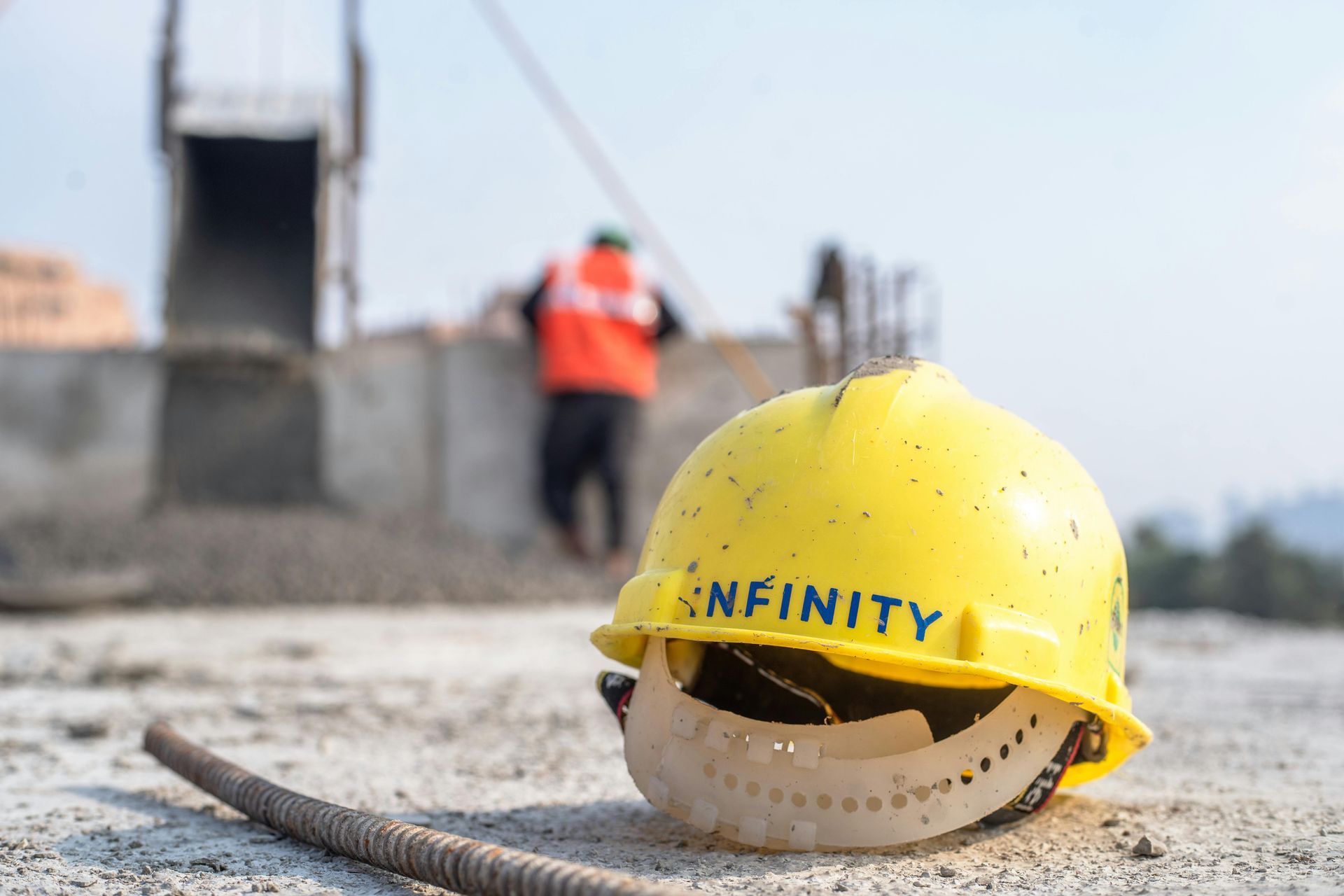 Yellow hard hat on a construction site with a blurred worker in an orange vest in the background