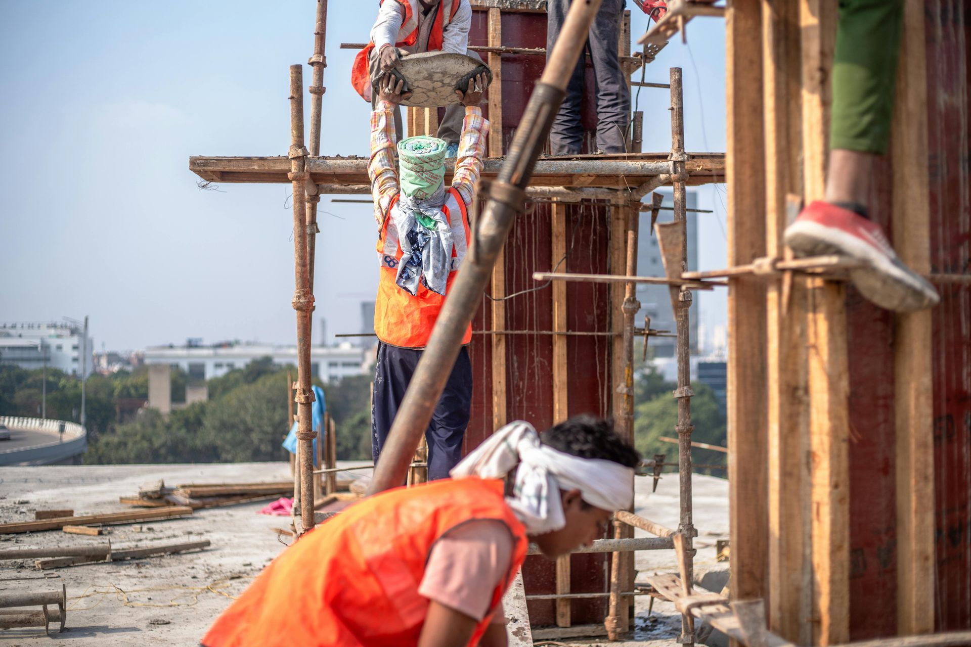Construction worker in orange vest on a bamboo scaffold, reaching near a tall decorated structure outdoors.
