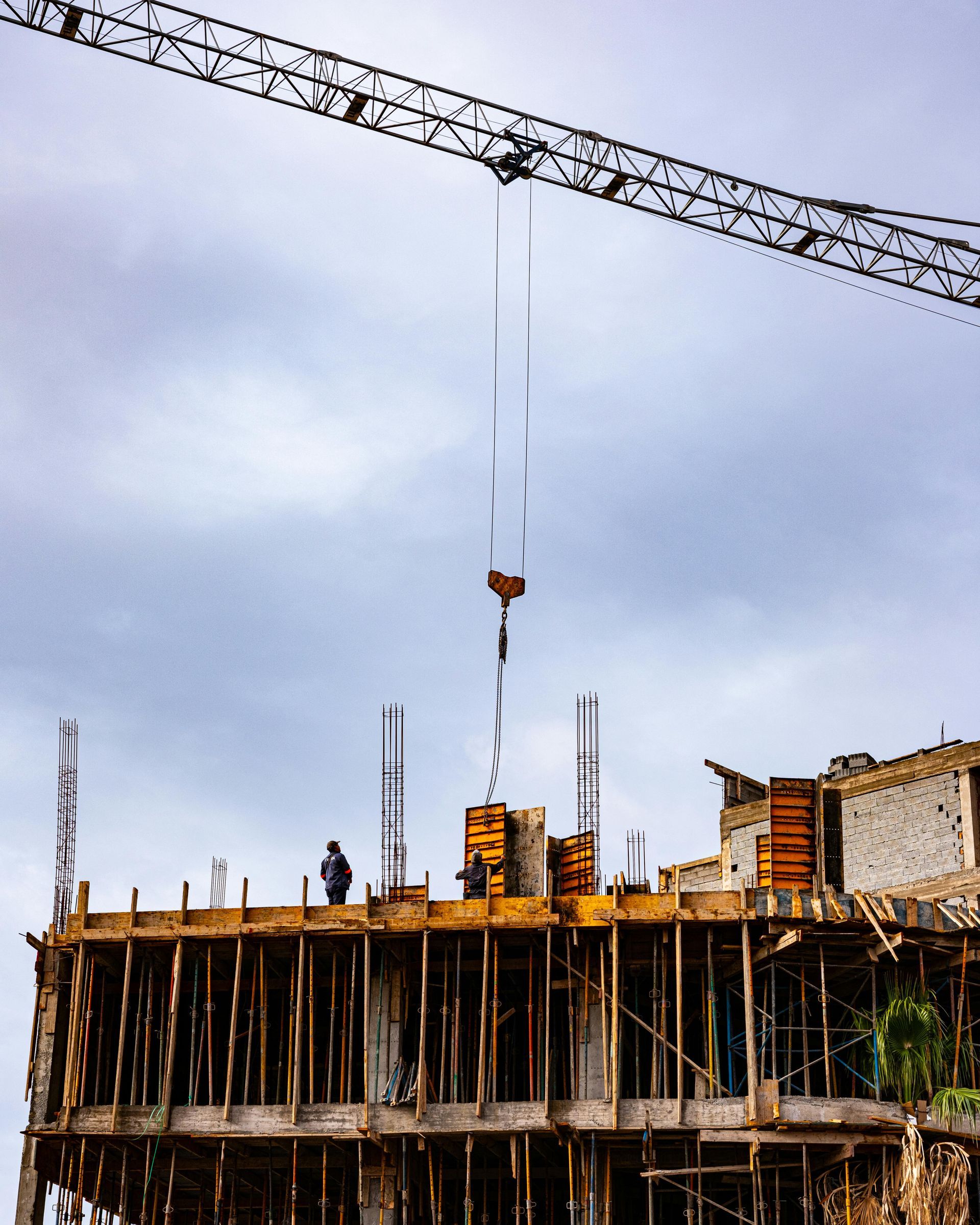 Construction site with a crane lifting materials over an unfinished concrete building under a cloudy sky
