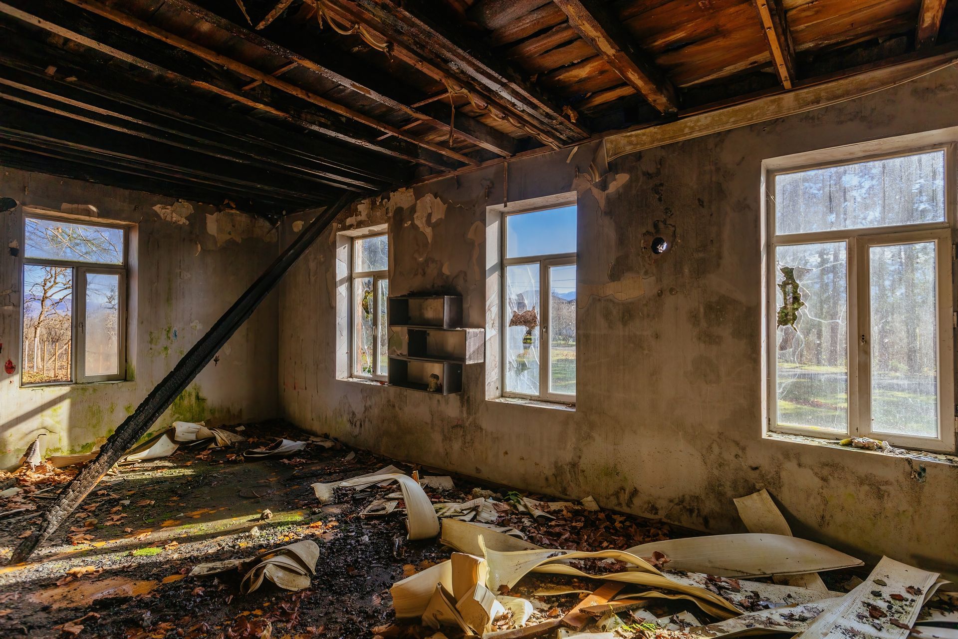 Dilapidated interior of a building with peeling paint, broken windows, and debris on the floor.