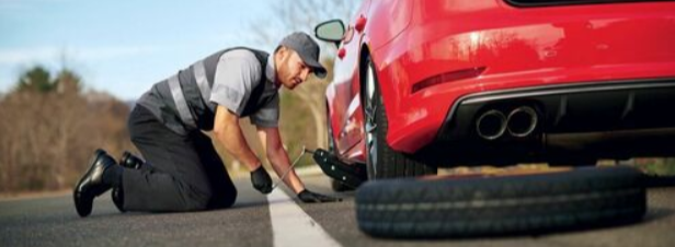 Burnaby Towing worker installing a spare tire on a red car using a car jack on the side of the road