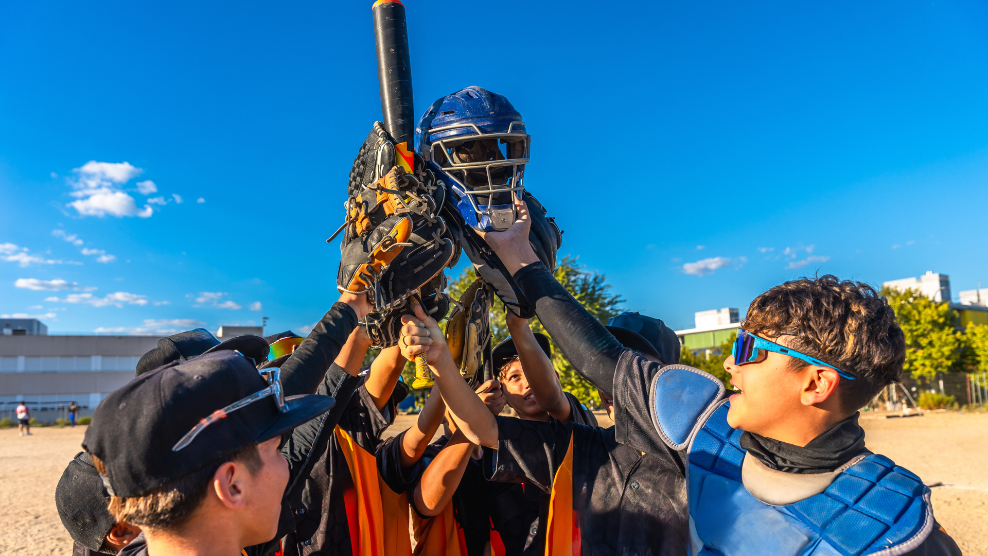 People in sports gear raising a trophy together outdoors under a bright blue sky