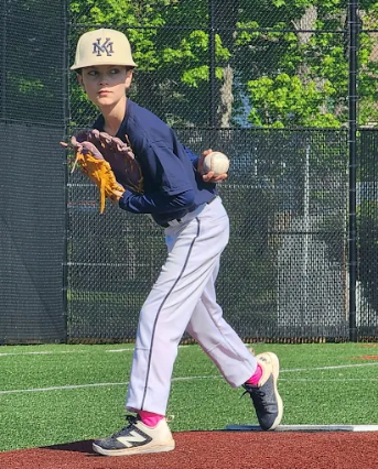 Three youth baseball players in navy jerseys and caps stand arm in arm on a grassy field.