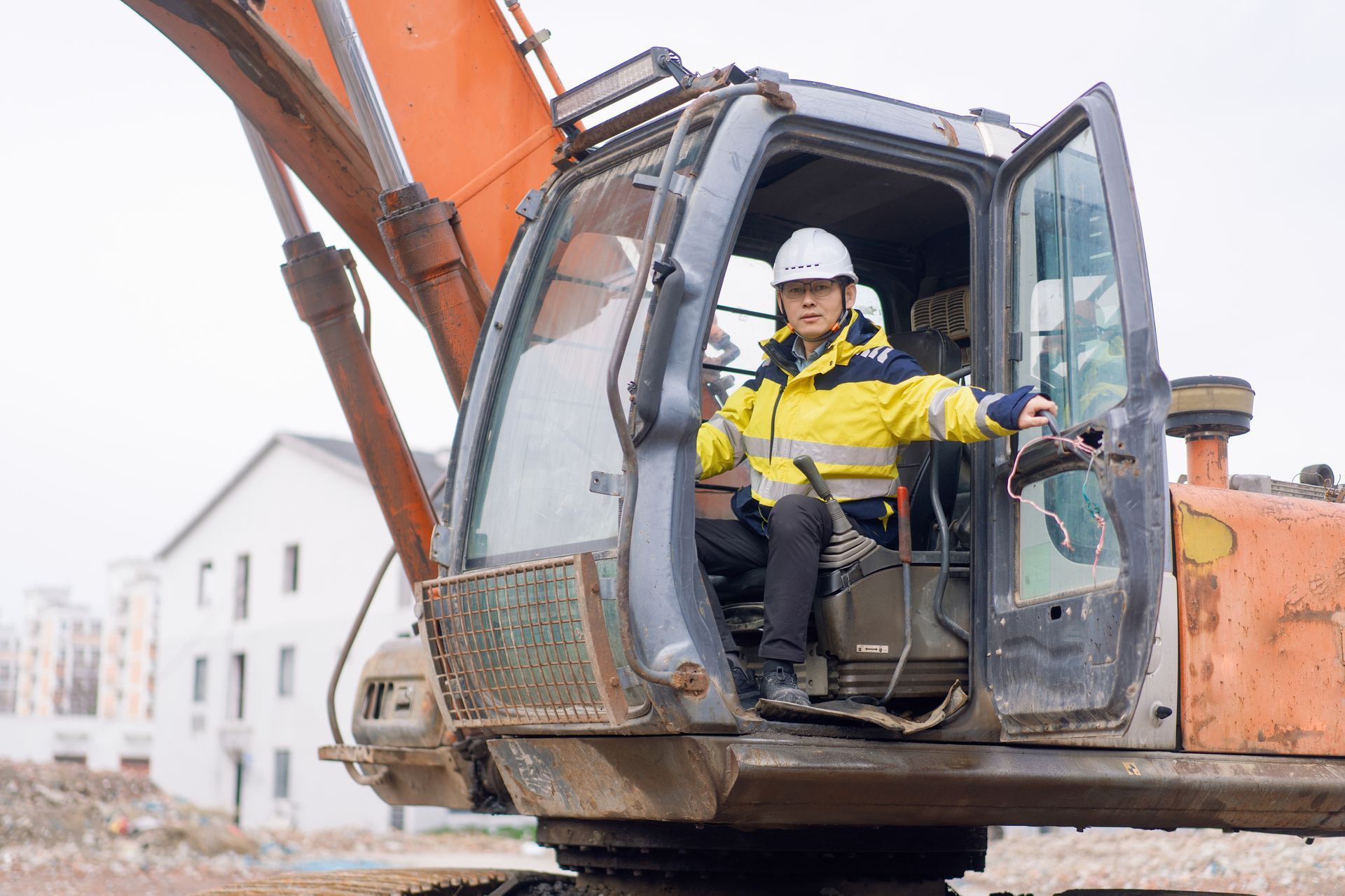 An excavator operator wearing a safety helmet and reflective jacket operating heavy machinery.