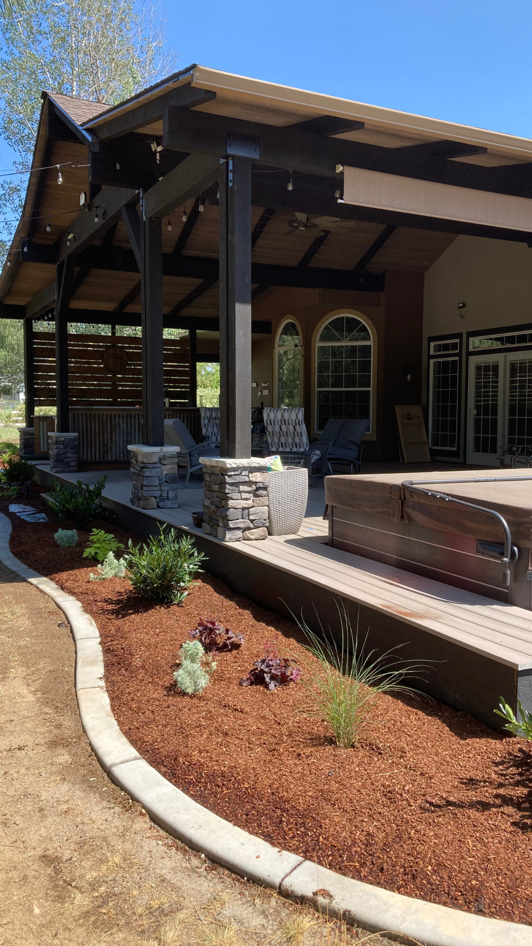 Exterior of a home with a covered patio, landscaping with red mulch and stonework; sunny day.