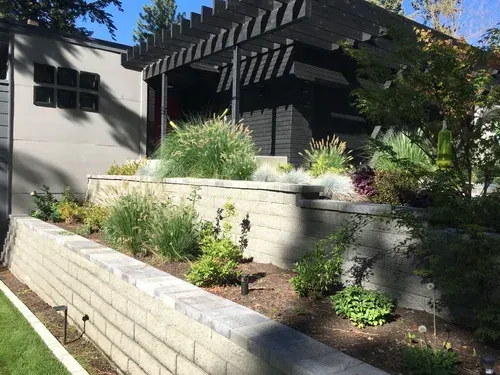 A tiered garden with retaining walls, plants, and a black pergola.