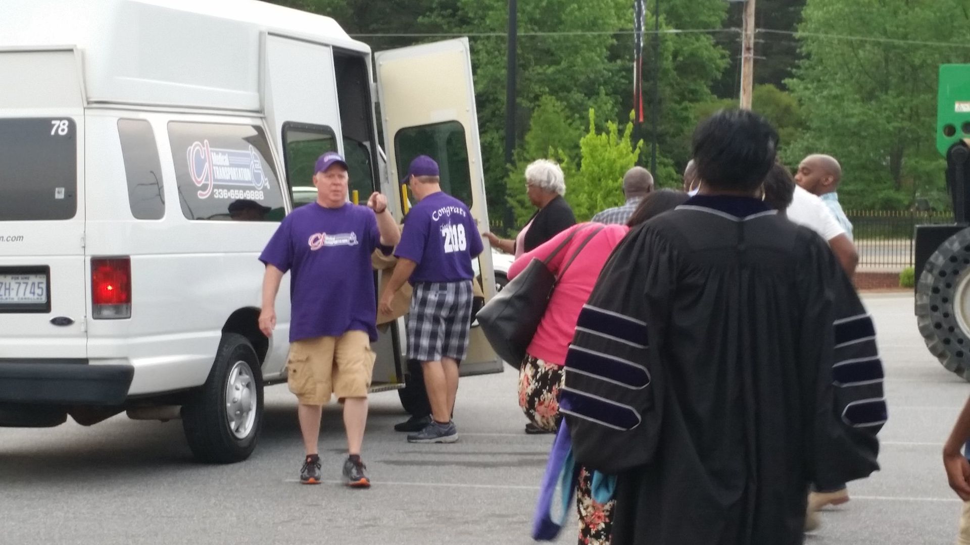 People unloading items from a white van; one person in a purple shirt and khaki shorts. 