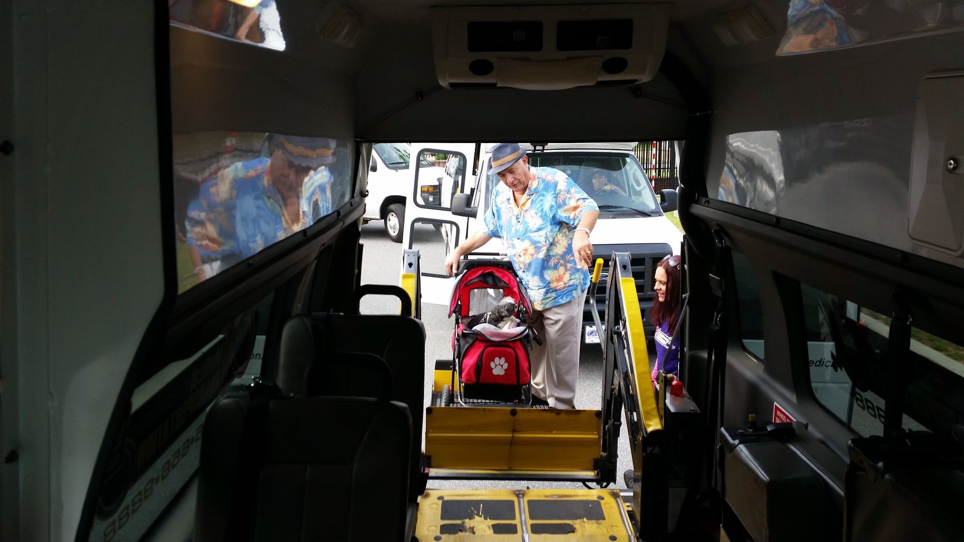Interior of accessible van; person assists child in a stroller onto a wheelchair lift.