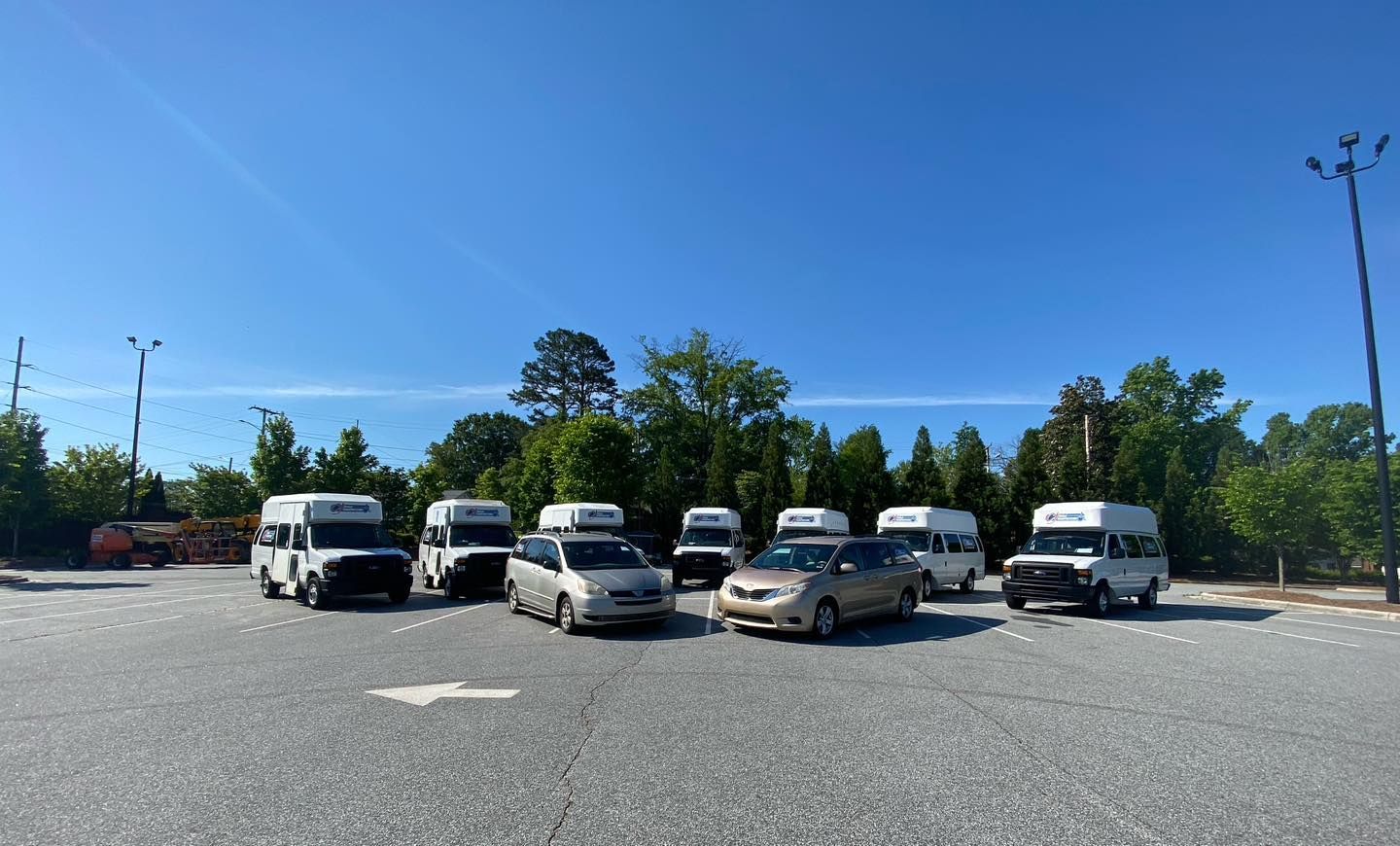A group of vans and cars parked on a gray asphalt lot on a sunny day.
