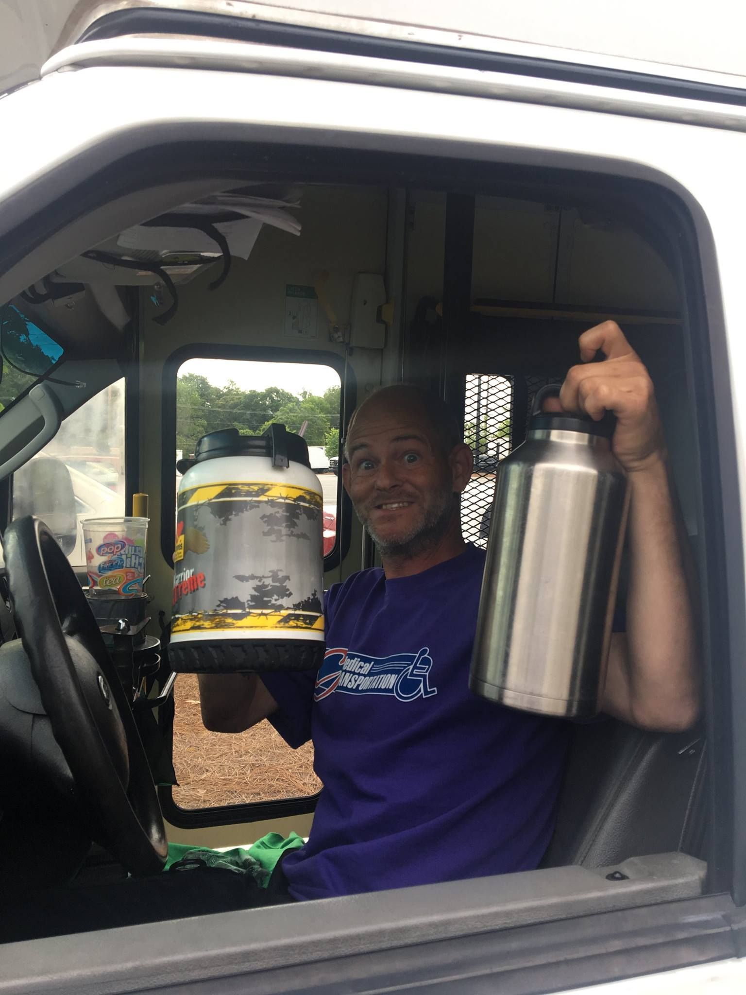 Man in vehicle holds a large water jug and a stainless steel bottle, smiling.