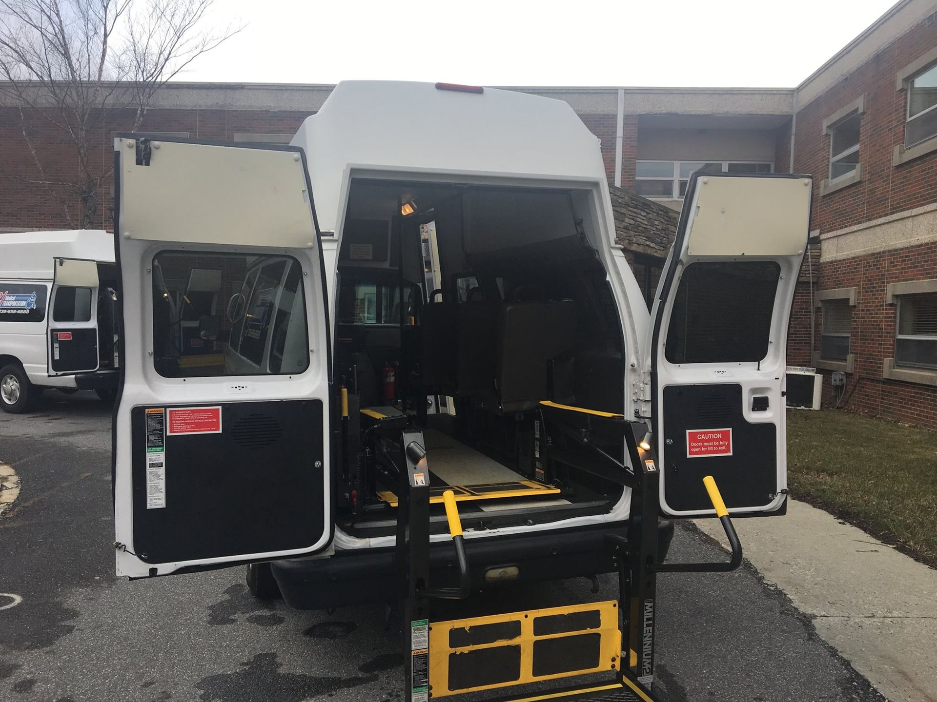 White van with open rear doors, accessible ramp extended.