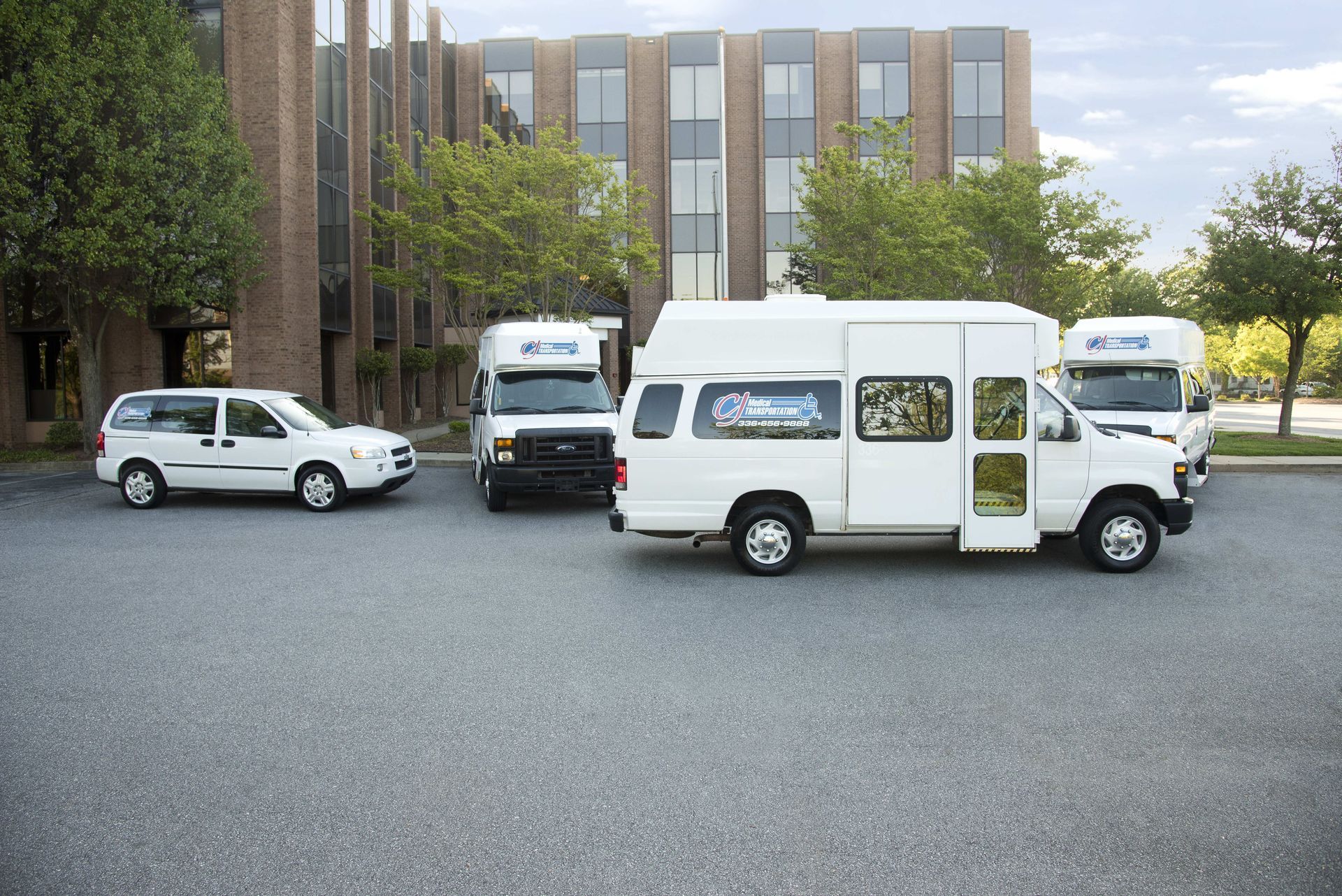 Several white vans and a car parked in a lot in front of a building.