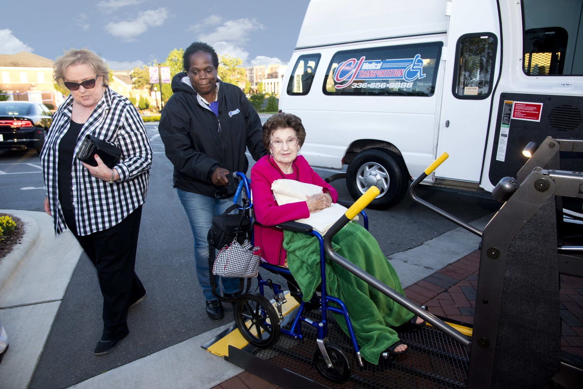 Woman in wheelchair being helped onto a van's lift by a person.