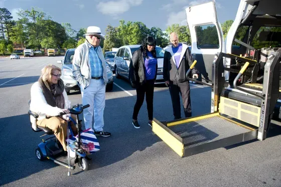 Person in scooter, three others near van with ramp open in parking lot. Person in scooter, three others near van with ramp open in parking lot.