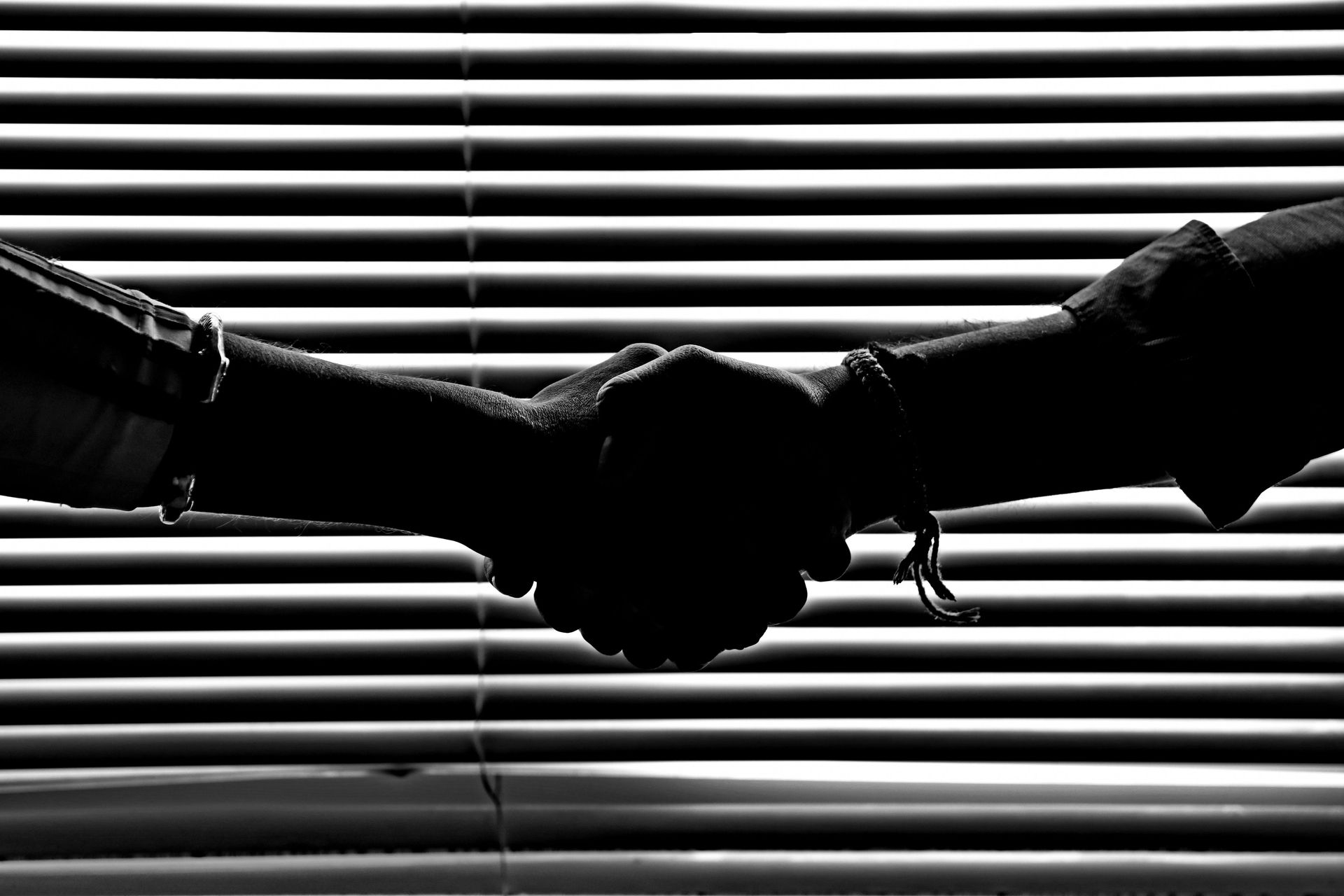 Two people shaking hands in silhouette against horizontal window blinds
