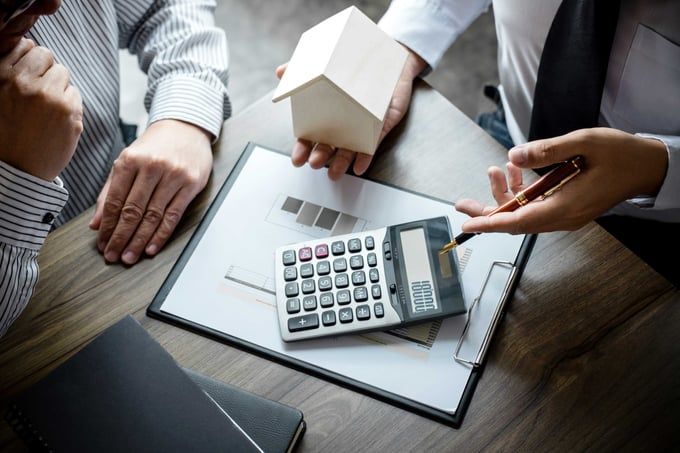 Hands reviewing house model and calculator on a clipboard during a financial meeting