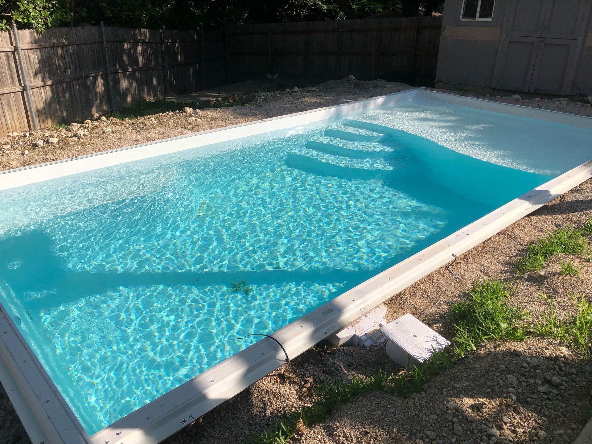 Rectangular outdoor swimming pool with clear blue water beside a grassy yard and wooden fence
