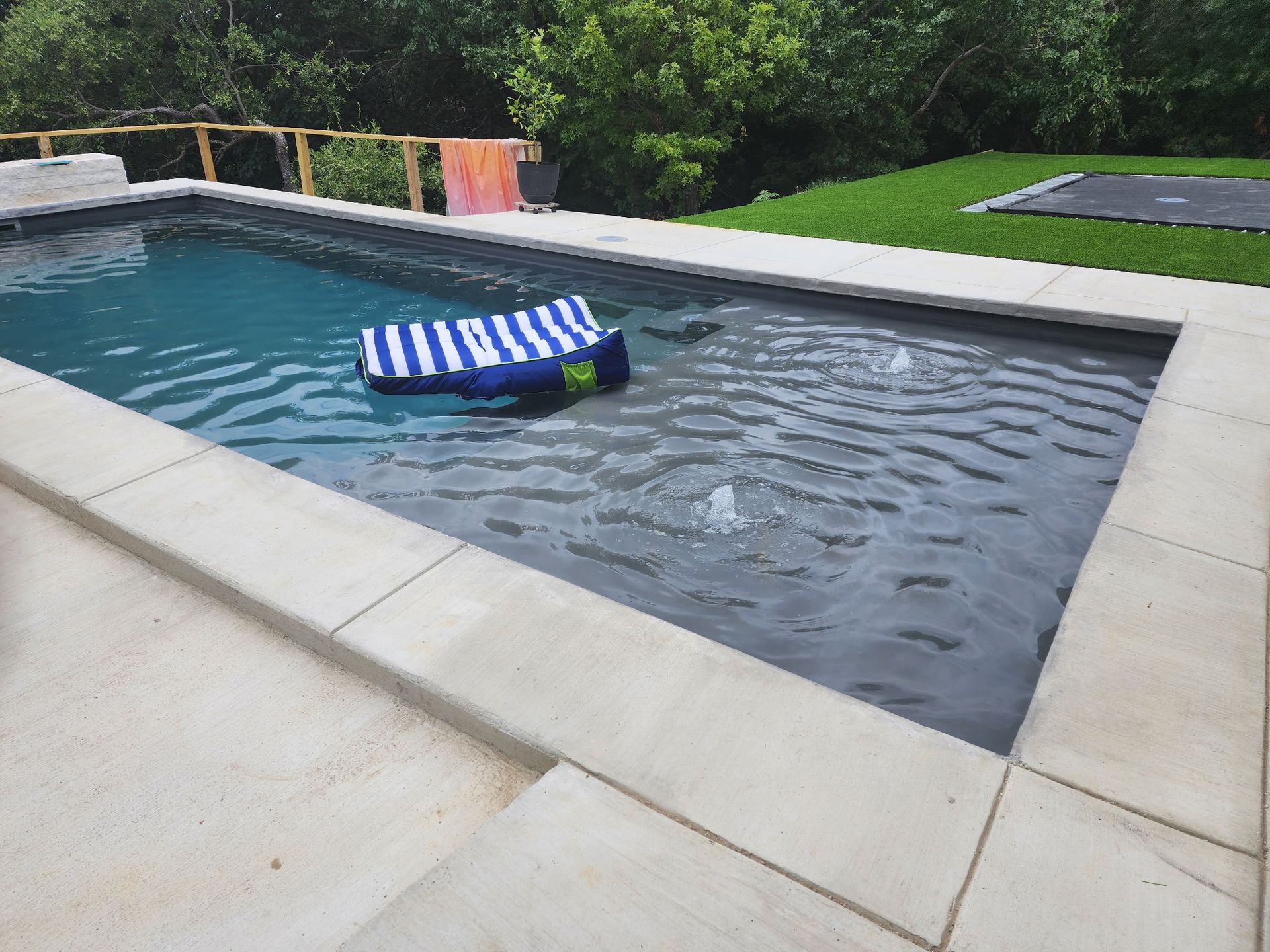 Backyard pool with a striped float drifting in the water and patio stones around it