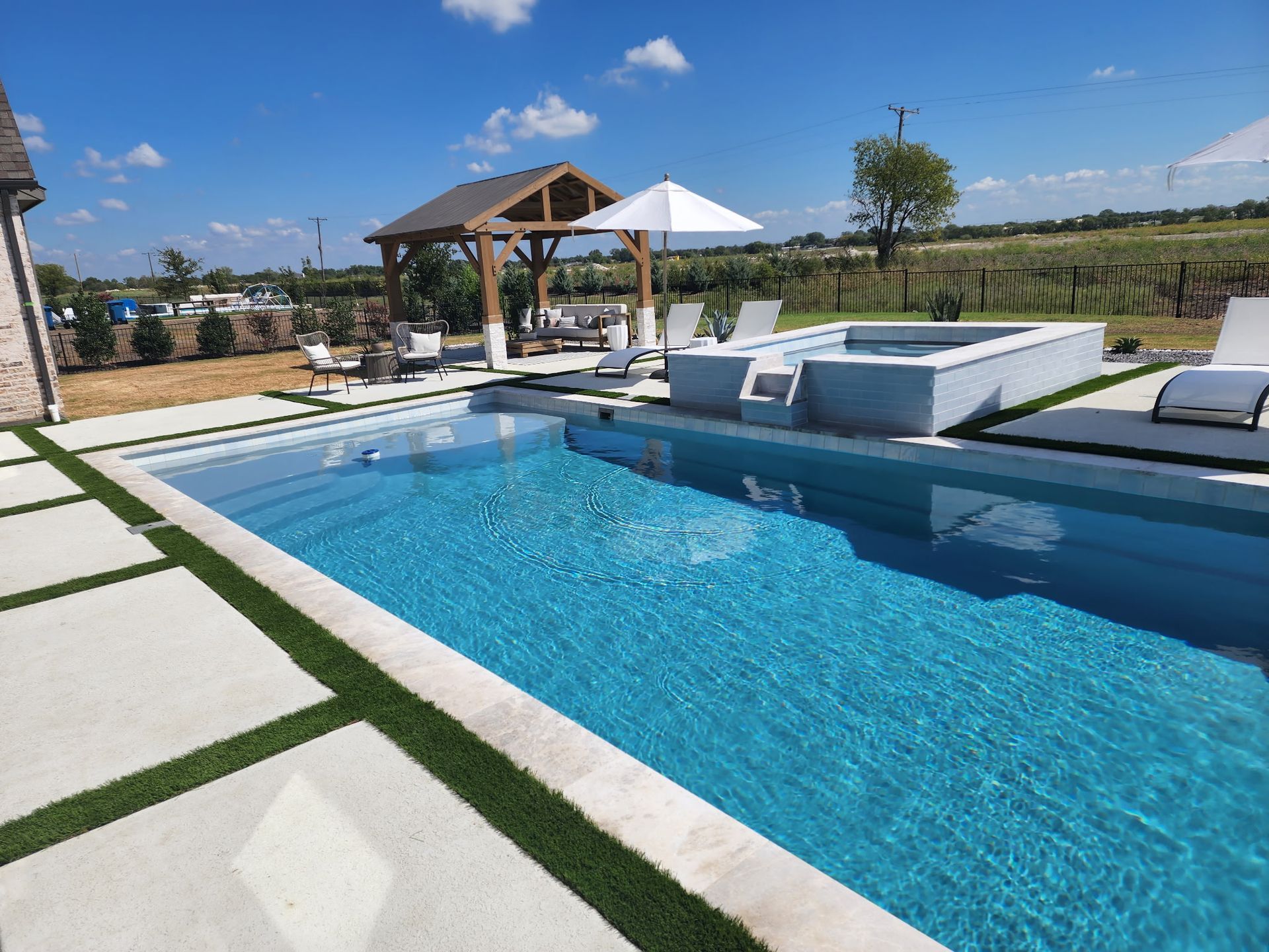 Modern backyard pool with blue water, white loungers, and a shaded patio under a sunny sky