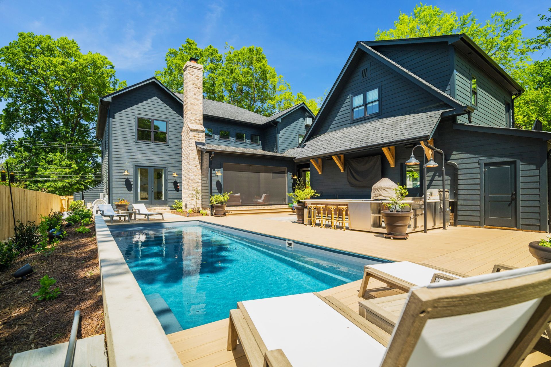 Modern backyard with black house, rectangular pool, and lounge chairs under bright sunlight