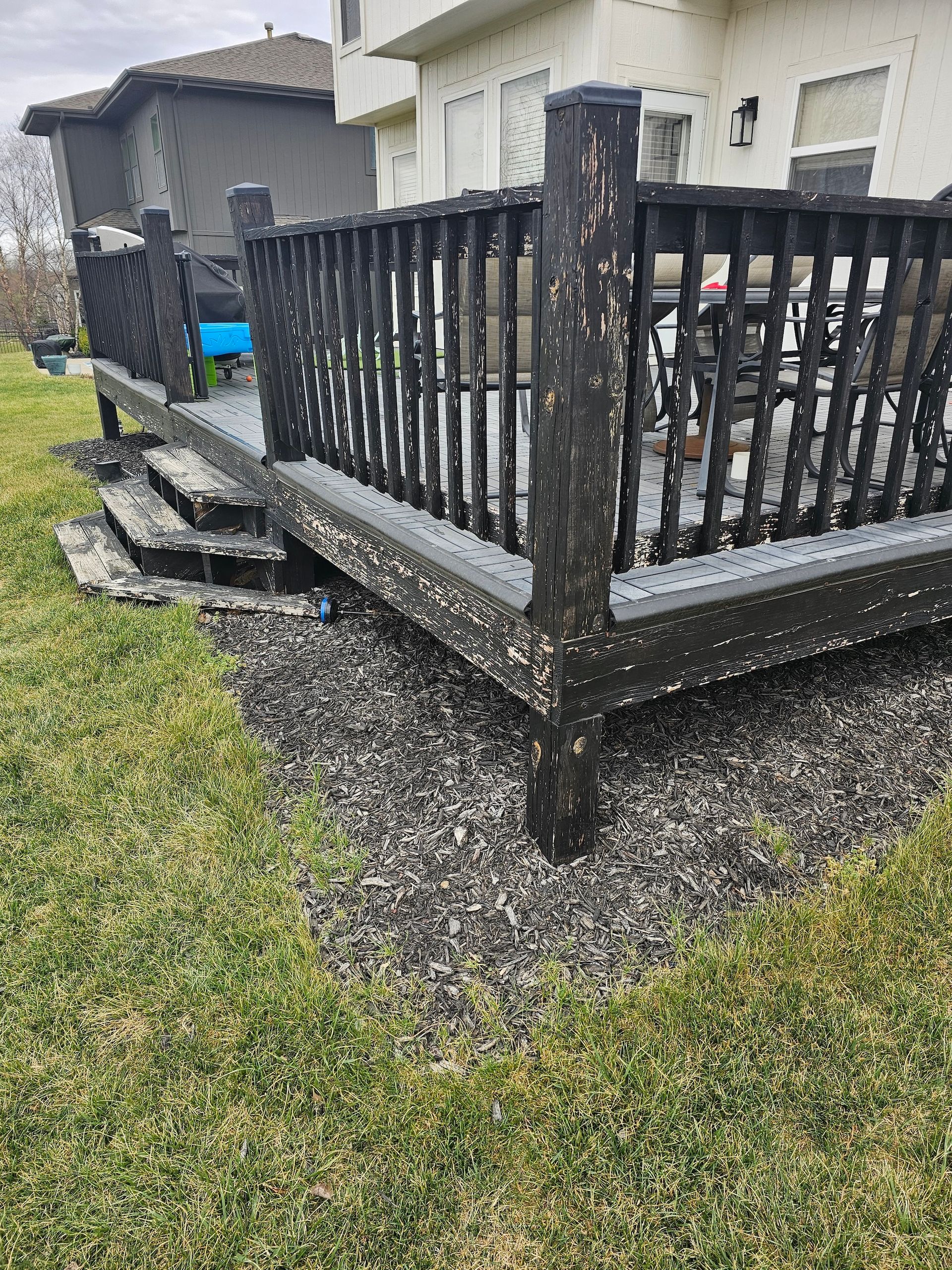 Backyard deck with black railing, gravel border, and stone steps beside a house