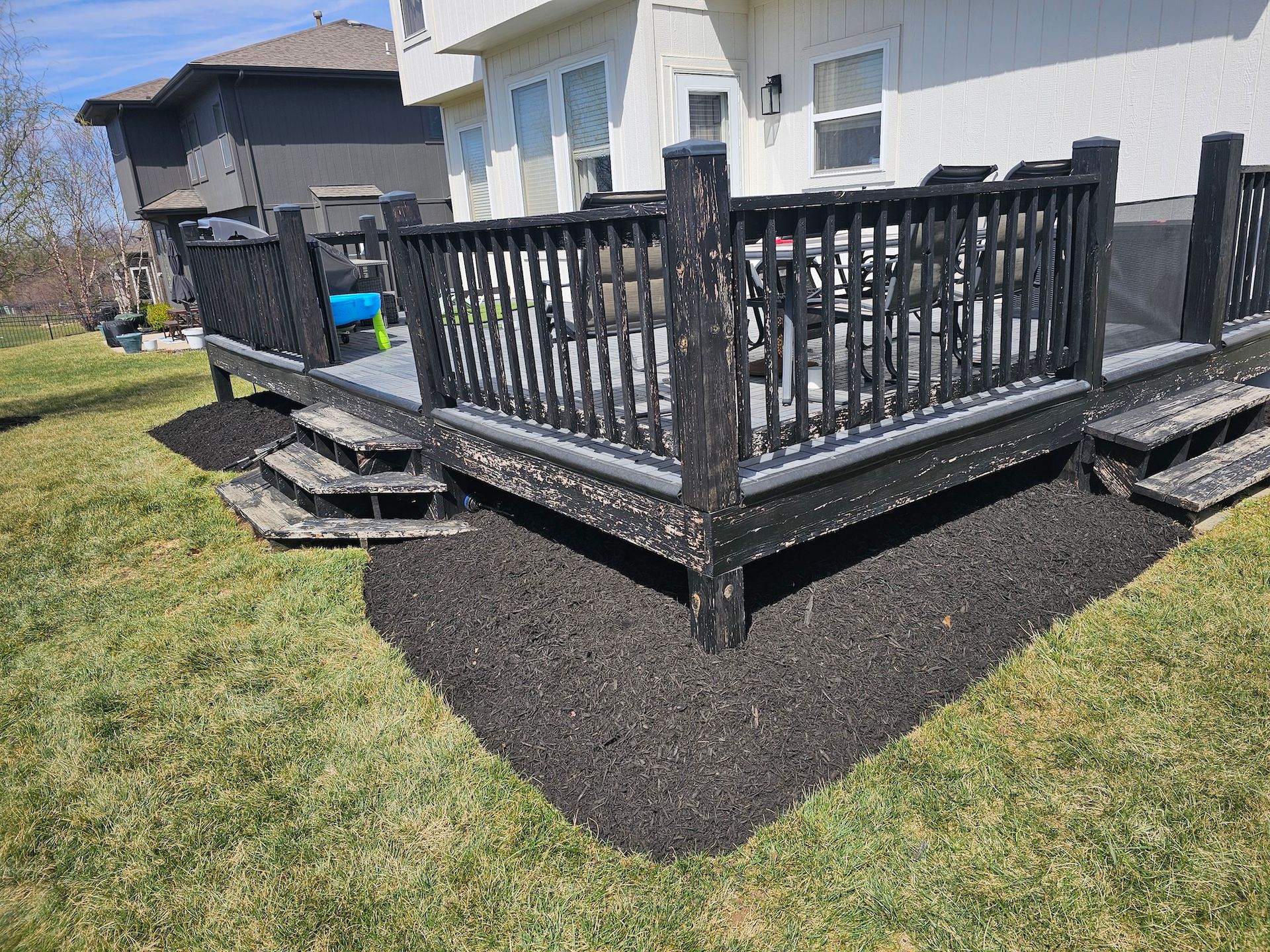 Black wooden deck with stairs and railings beside a white house in a backyard under construction