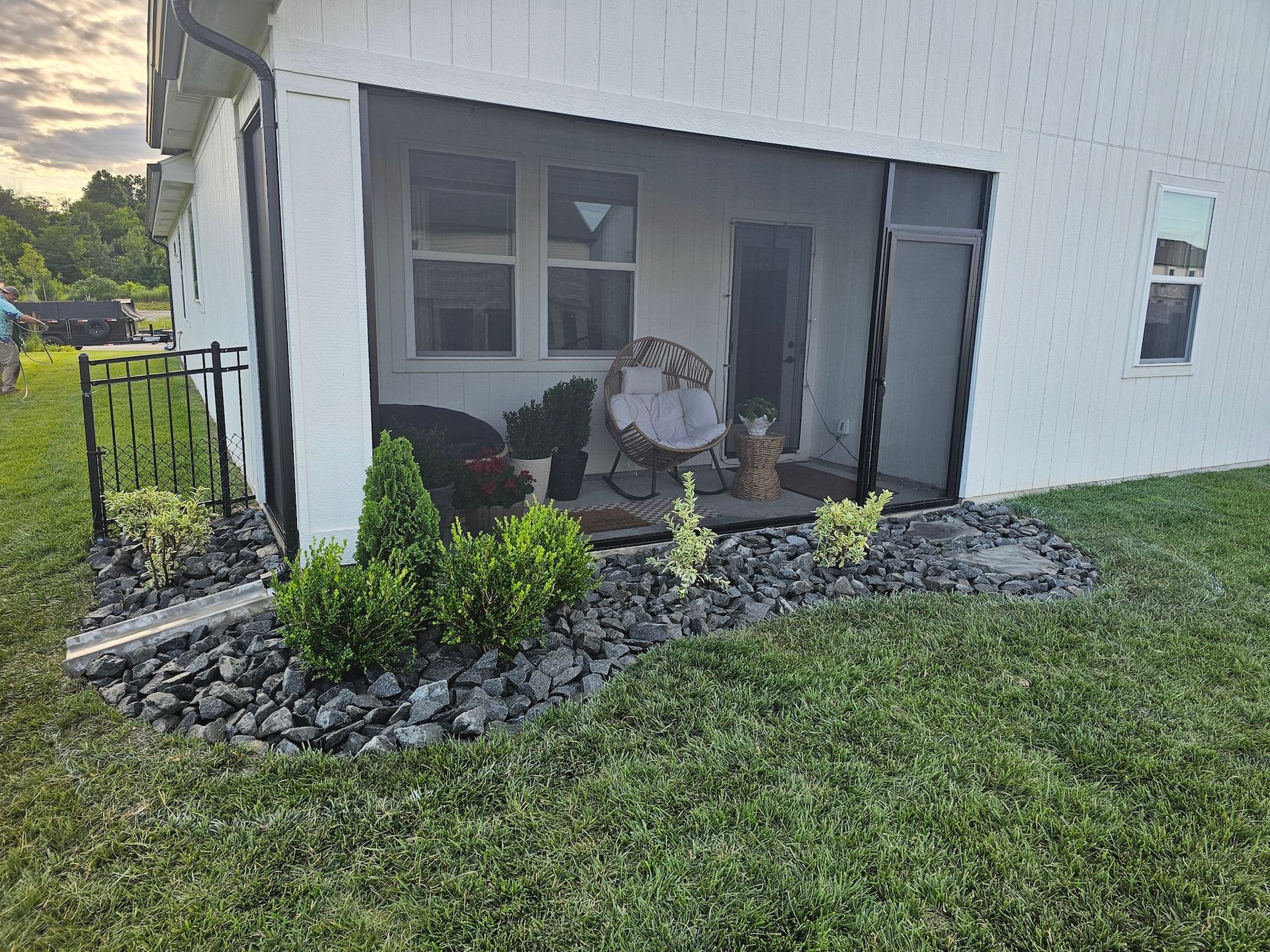Small screened porch with outdoor chairs beside a white house and landscaped rock garden.