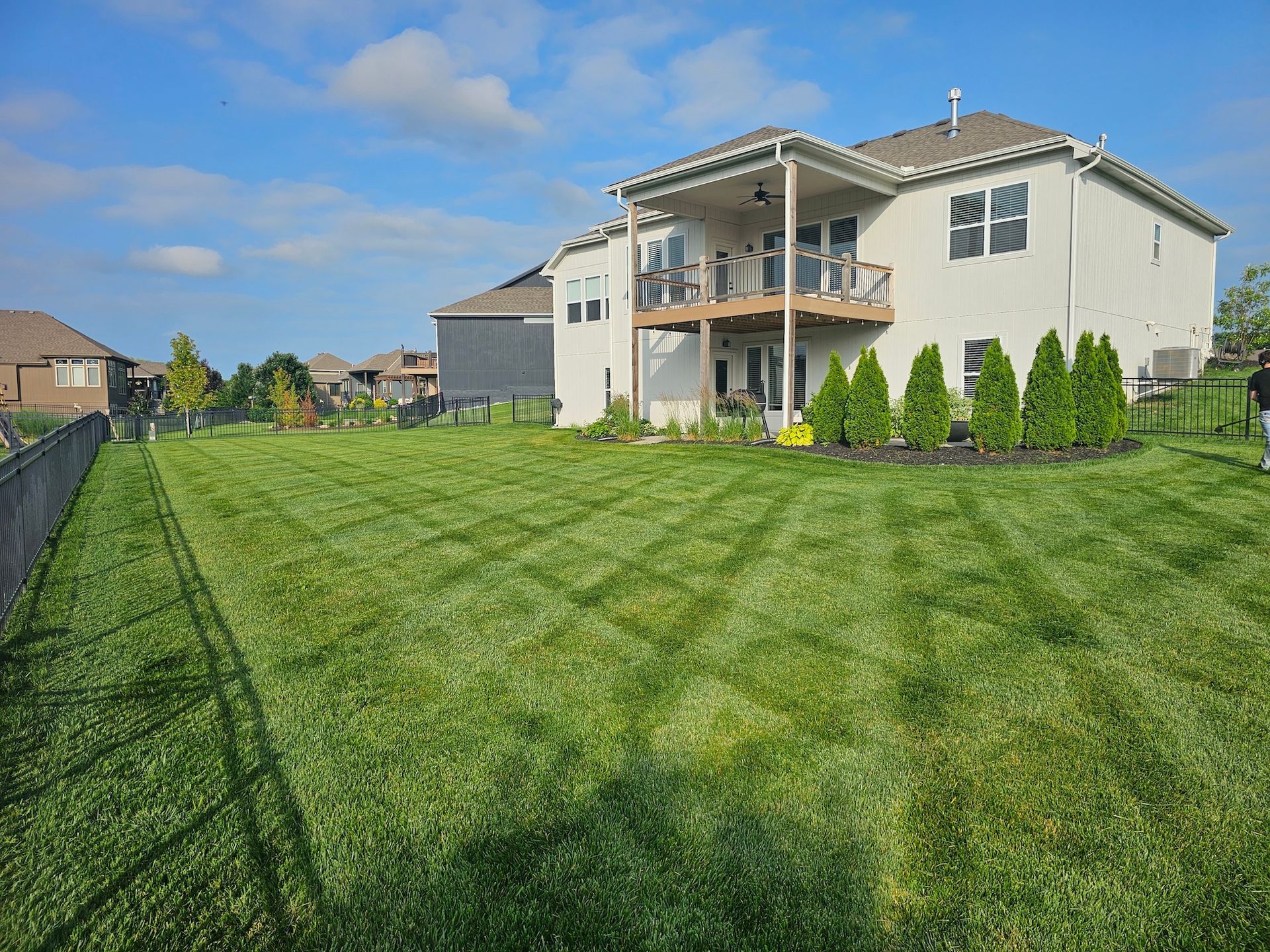 Backyard with green lawn and a two-story house with a balcony on a sunny day