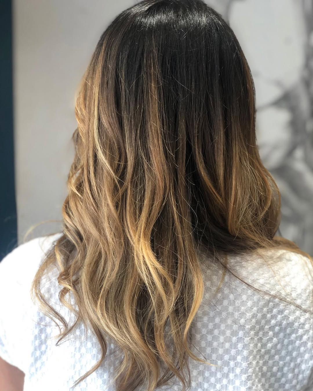 Vista posteriore di lunghi capelli castani mossi con mèches bionde, sopra un top bianco testurizzato
