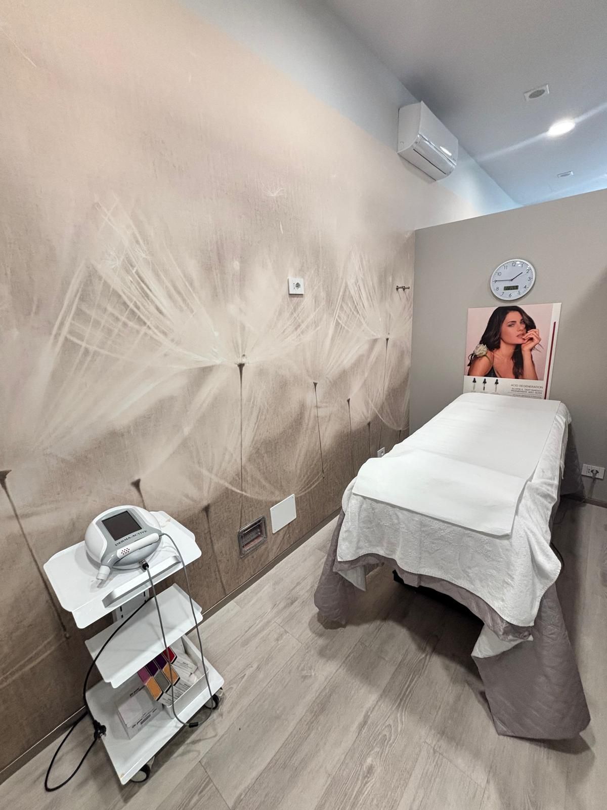 Cabina per trattamenti spa con lettino da massaggio, murale a parete e attrezzatura per trattamenti viso su un carrello.