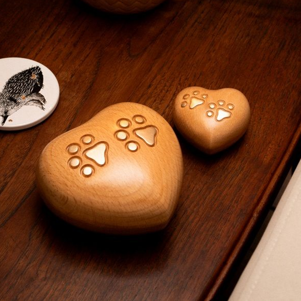 Two wooden heart-shaped pet urns with paw print engravings on a dark wooden surface.