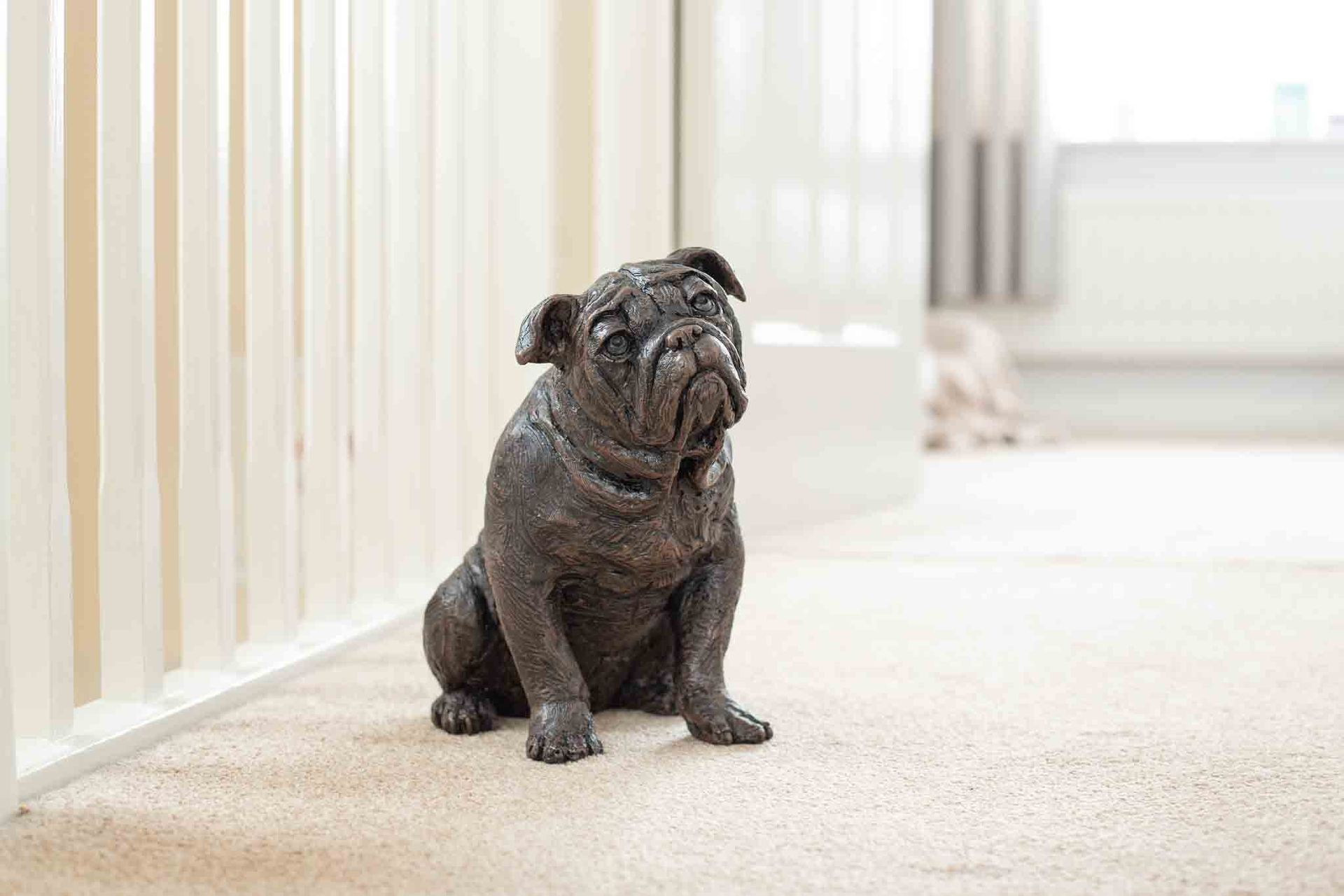 Statue of a bulldog sitting on a beige carpet next to a white bannister.