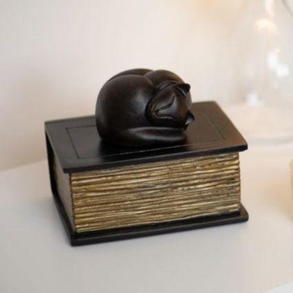 Black cat figurine curled on a closed, black book with gold-edged pages.
