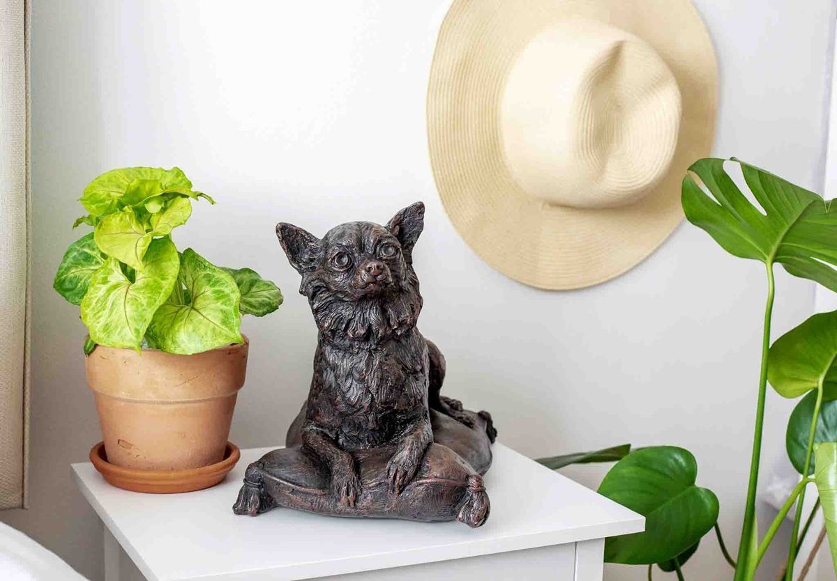 Dog statue on a white table, next to a potted plant and a straw hat hanging on the wall.