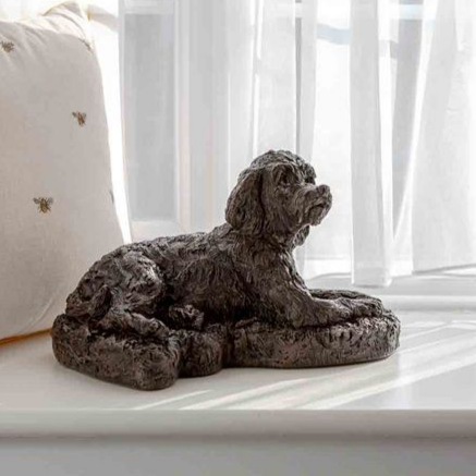 Dark brown dog statue resting on a windowsill, beside a white pillow and window.