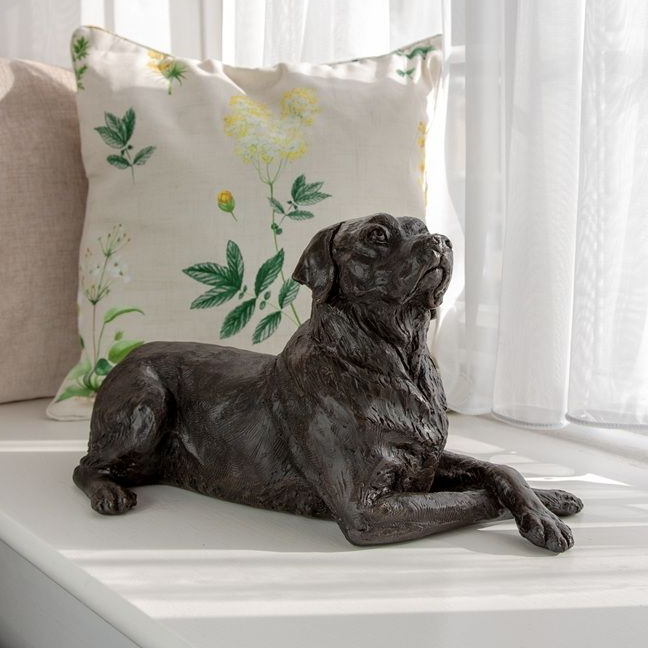 Bronze Labrador retriever statue resting on a windowsill, looking upwards, with a floral pillow.