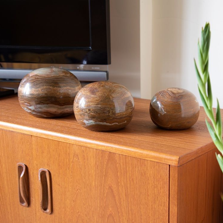 Three brown stone spheres on a wooden cabinet, in front of a black TV screen.
