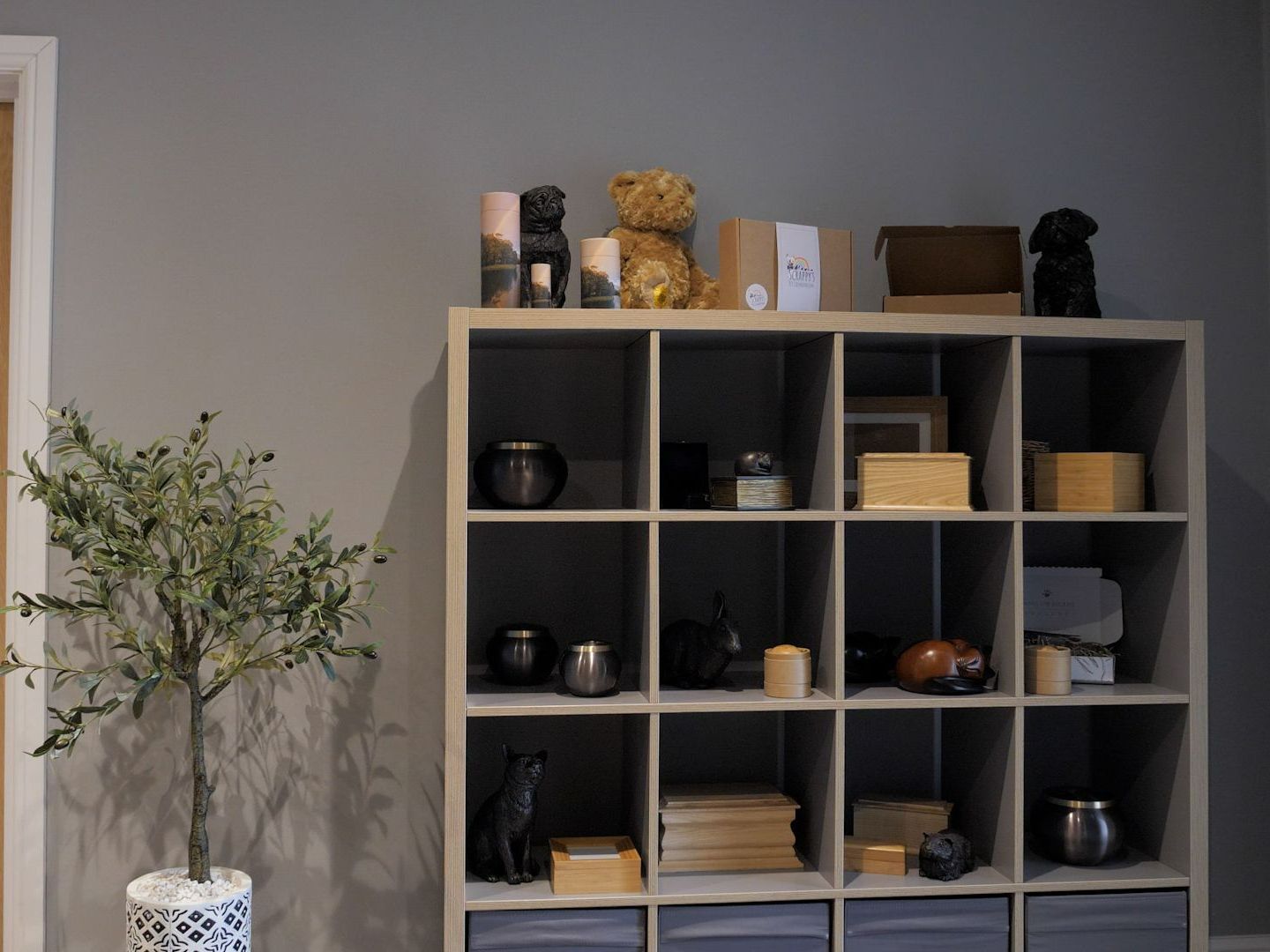 Gray cube storage unit with various decorative objects, including candles, boxes, and a teddy bear.