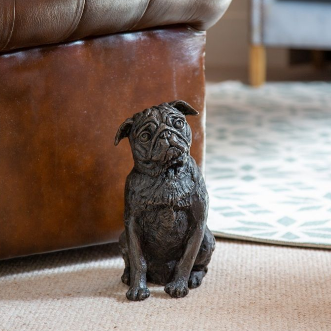 Bronze pug statue sitting on a carpet near a brown leather couch.