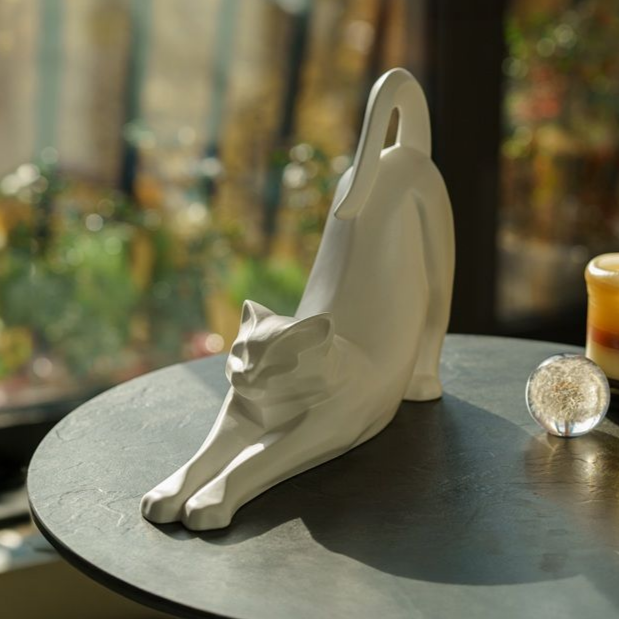 White cat sculpture stretching on a dark table, with a clear glass ball and blurred background.