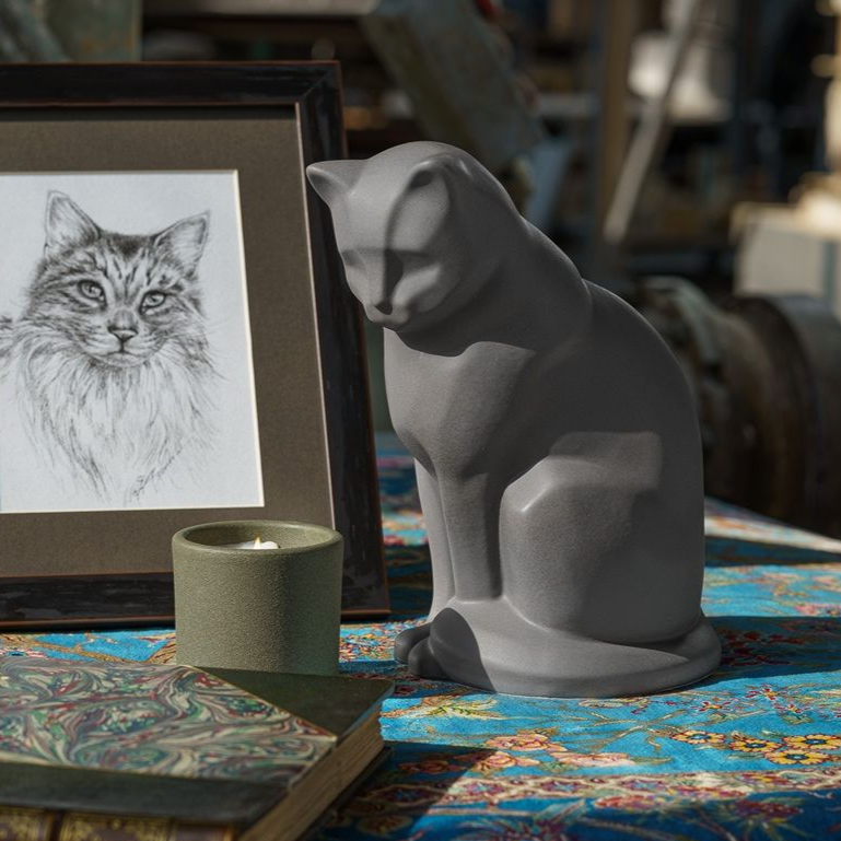 Gray cat statue and framed cat drawing on a table, next to a candle.