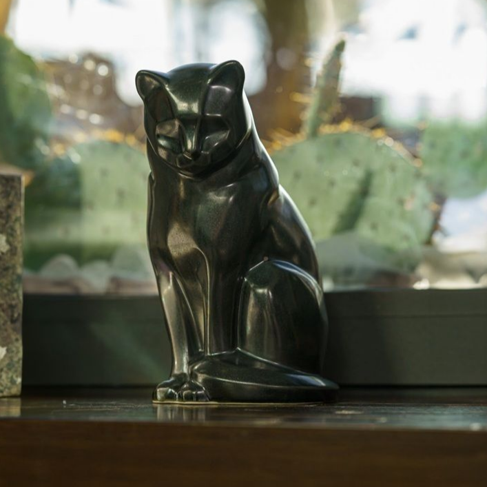 Bronze cat statue sitting on a wooden surface with a cactus in the background.