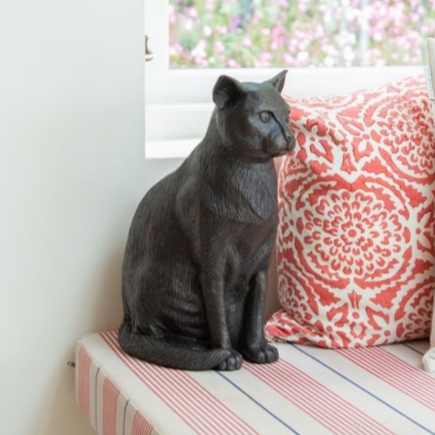 Black cat statue sitting on a striped bench with a red patterned pillow.