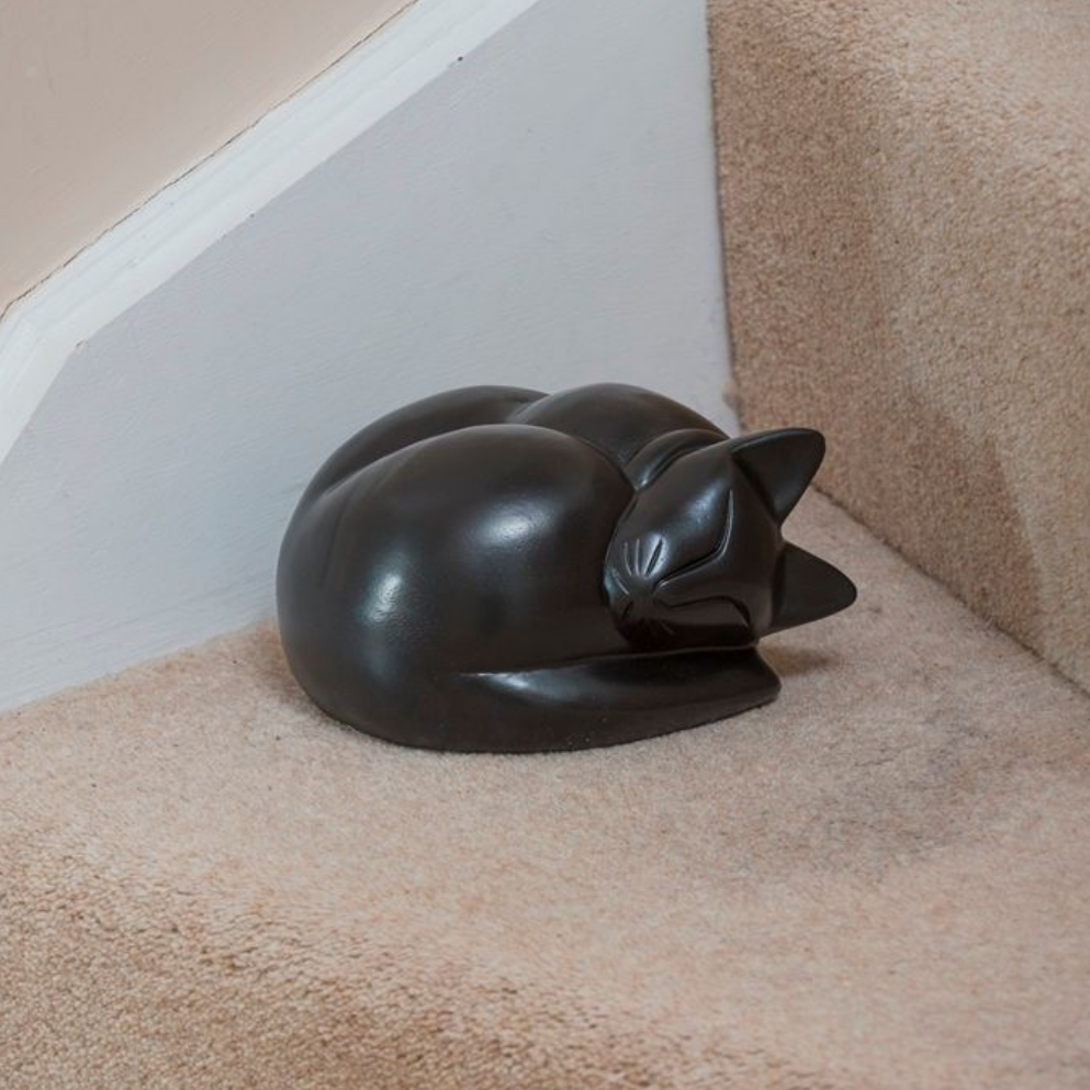 Black cat sculpture curled up on tan carpeted stairs.