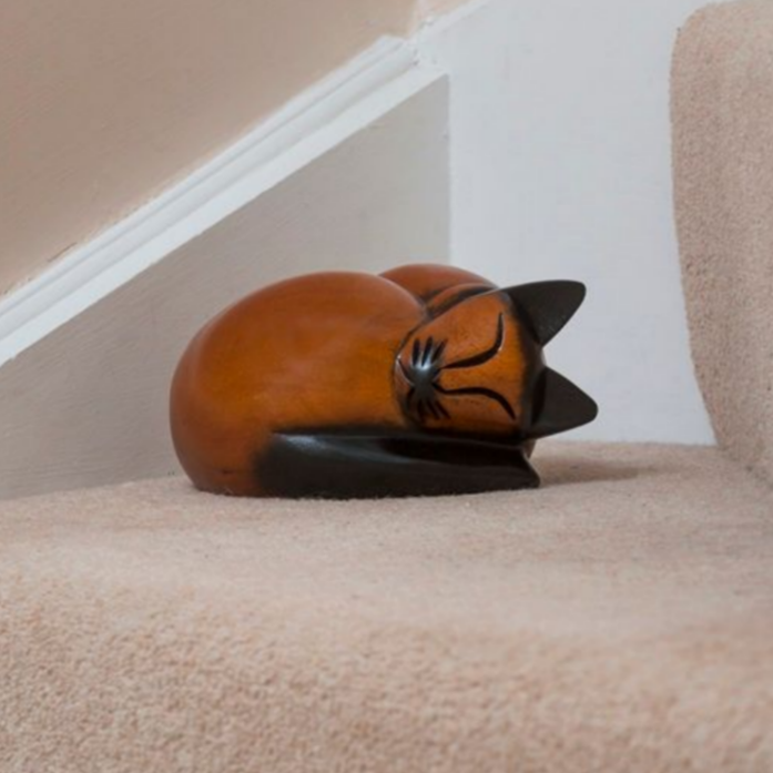 Wooden cat figurine curled up on a carpeted staircase step.