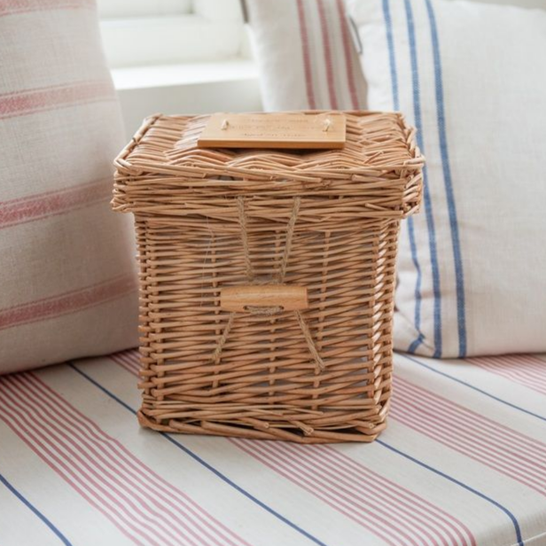 Wicker storage basket with a wooden lid and handle, sitting on a striped cushion.