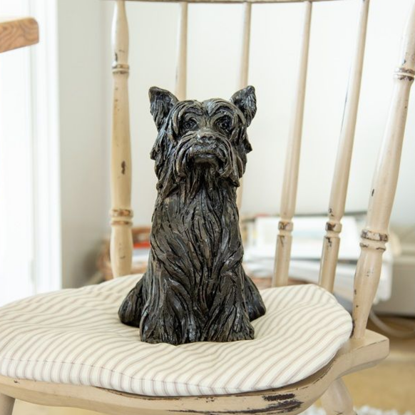 Bronze dog statue sitting on a striped cushion on a distressed wooden chair.