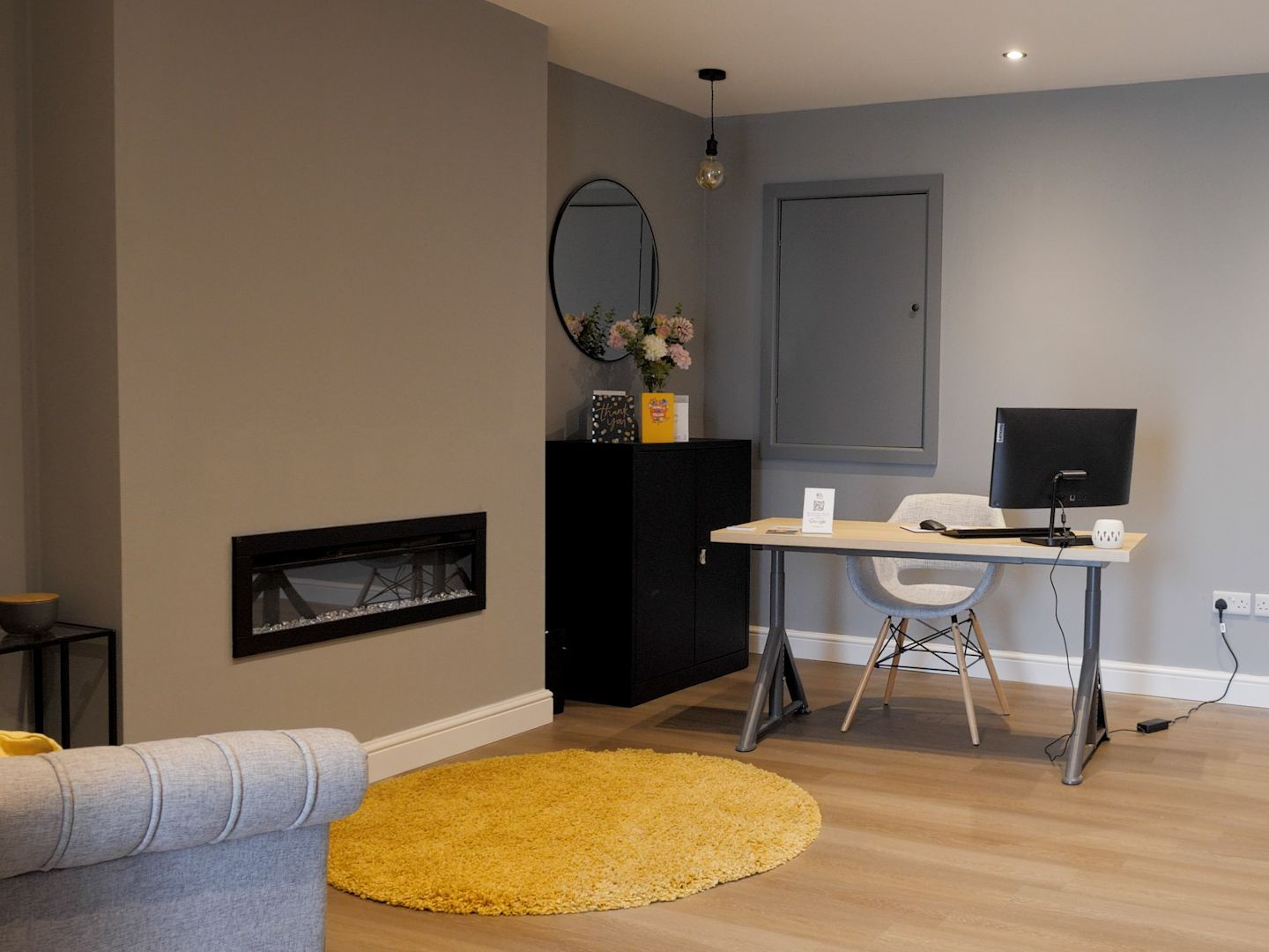 Modern office space with fireplace, desk, round yellow rug, and black cabinet. Gray walls.